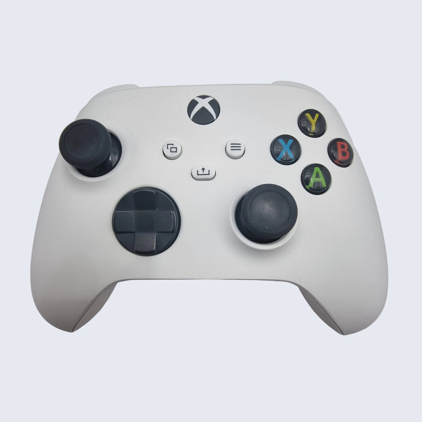 White gaming controller with black buttons on a light gray background